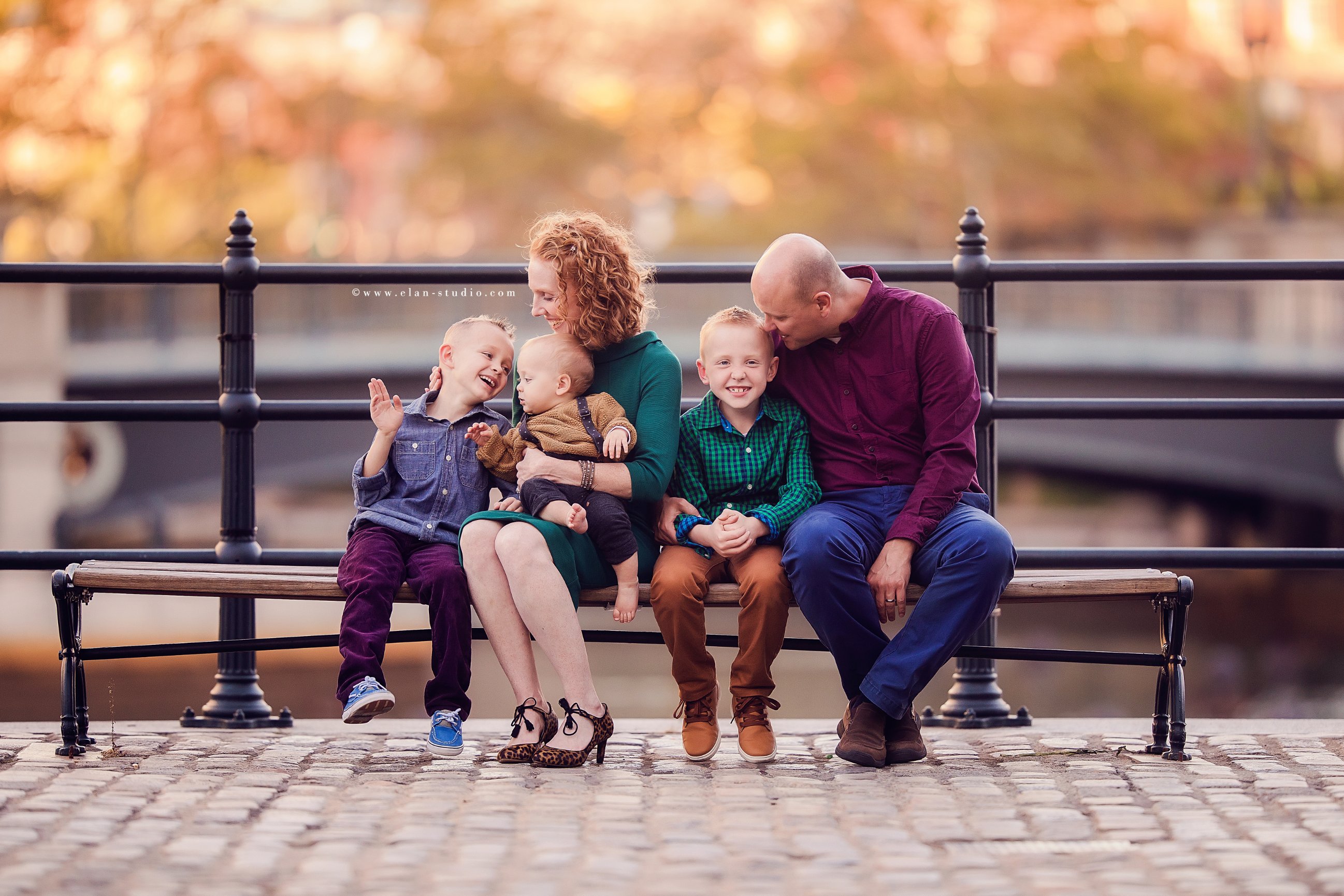 family sitting on city park bench with fall color in background, by Tracy Sweeney