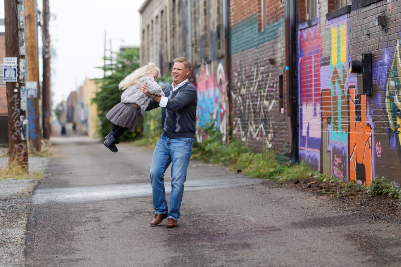 Dad swinging daughter around having fun on Denver Colorado Street with graffiti.