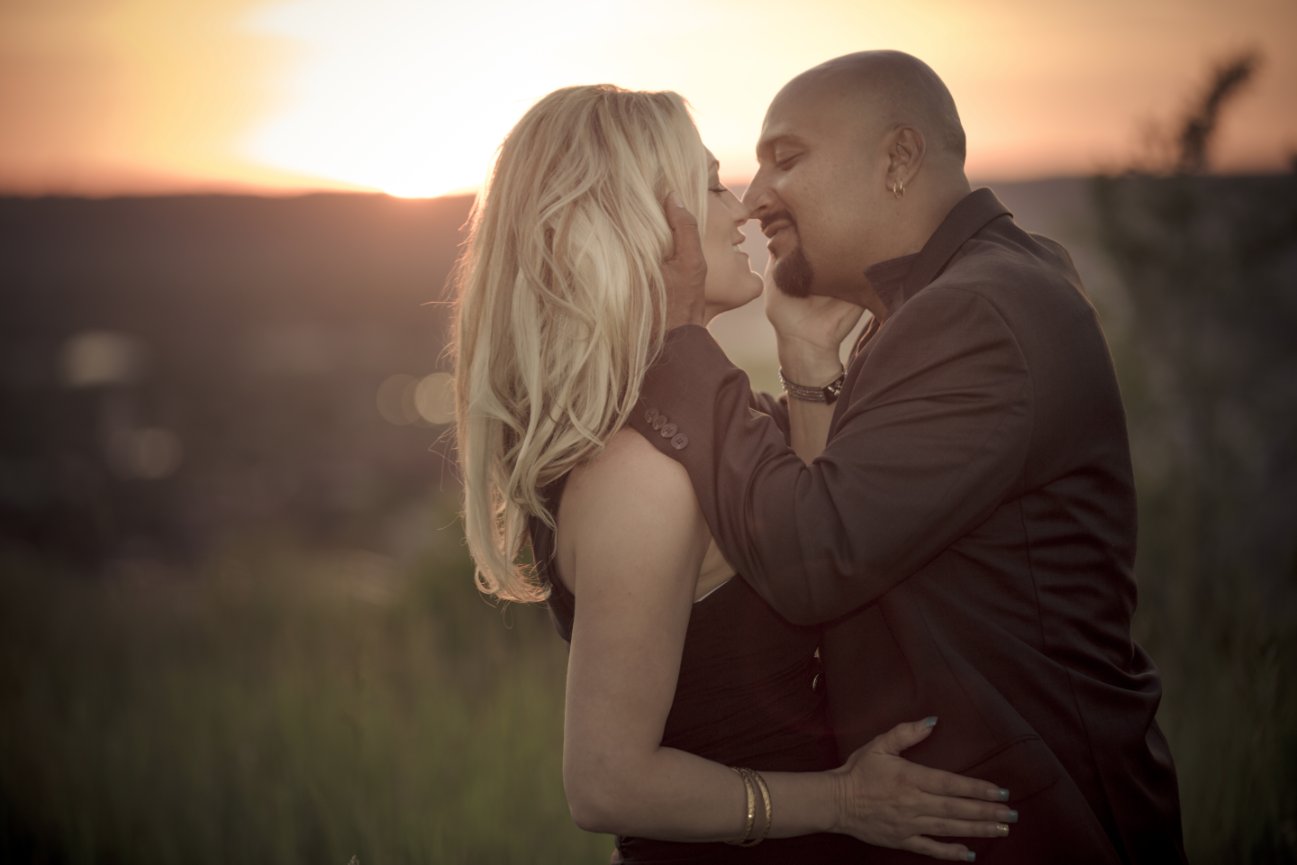 Couple embracing at sunset in a grassy field, creating a romantic atmosphere. Hamilton Mountain brow