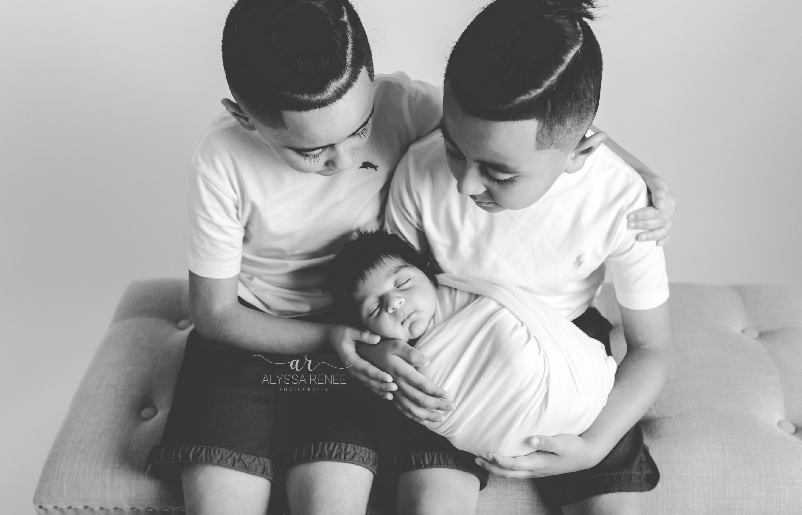  black and white photo of Brothers holding newborn baby sitting on bench in our jacksonville florida studio