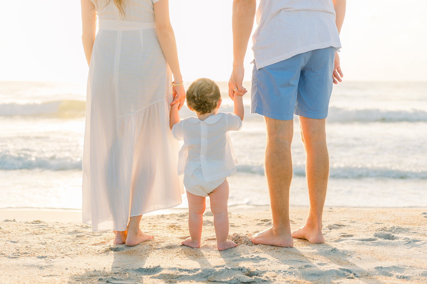 mom and dad holding one year-old son's hands, looking out at the Atlantic ocean