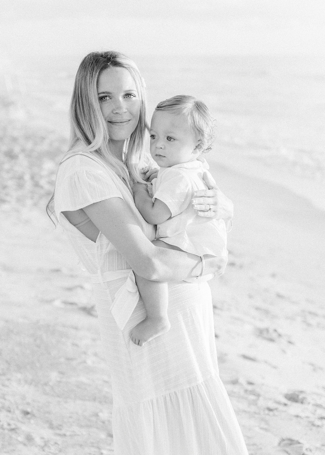 light and airy black and white photograph of a mother and her one year old son on the beach