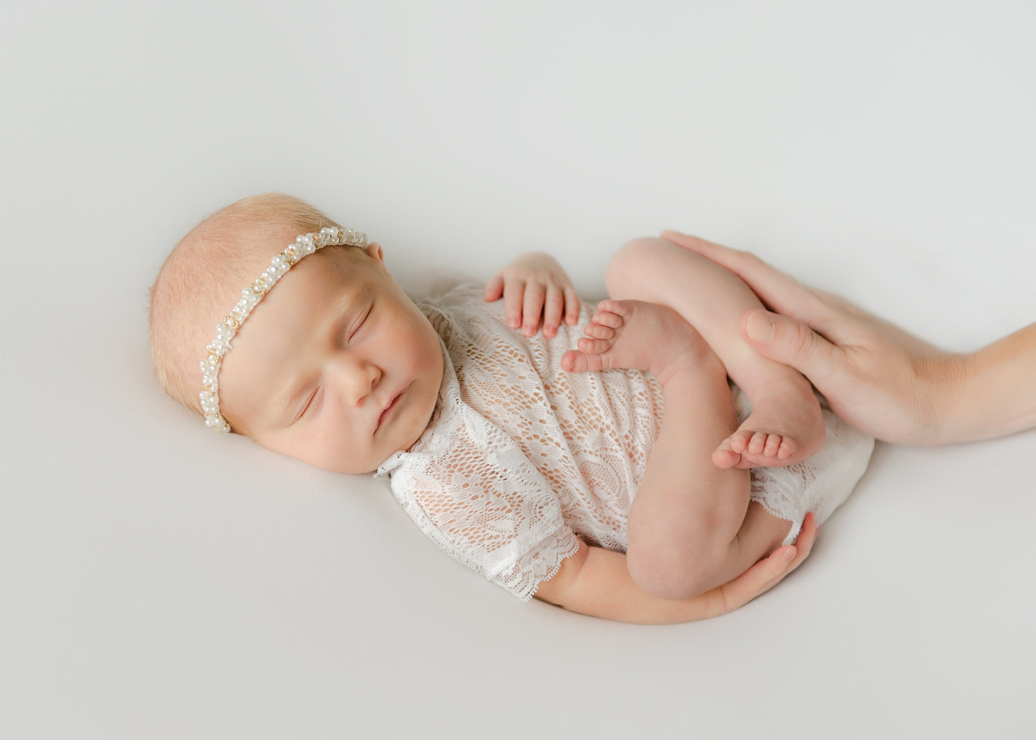 newborn baby girl wearing a lace onesie and an eyelet headband