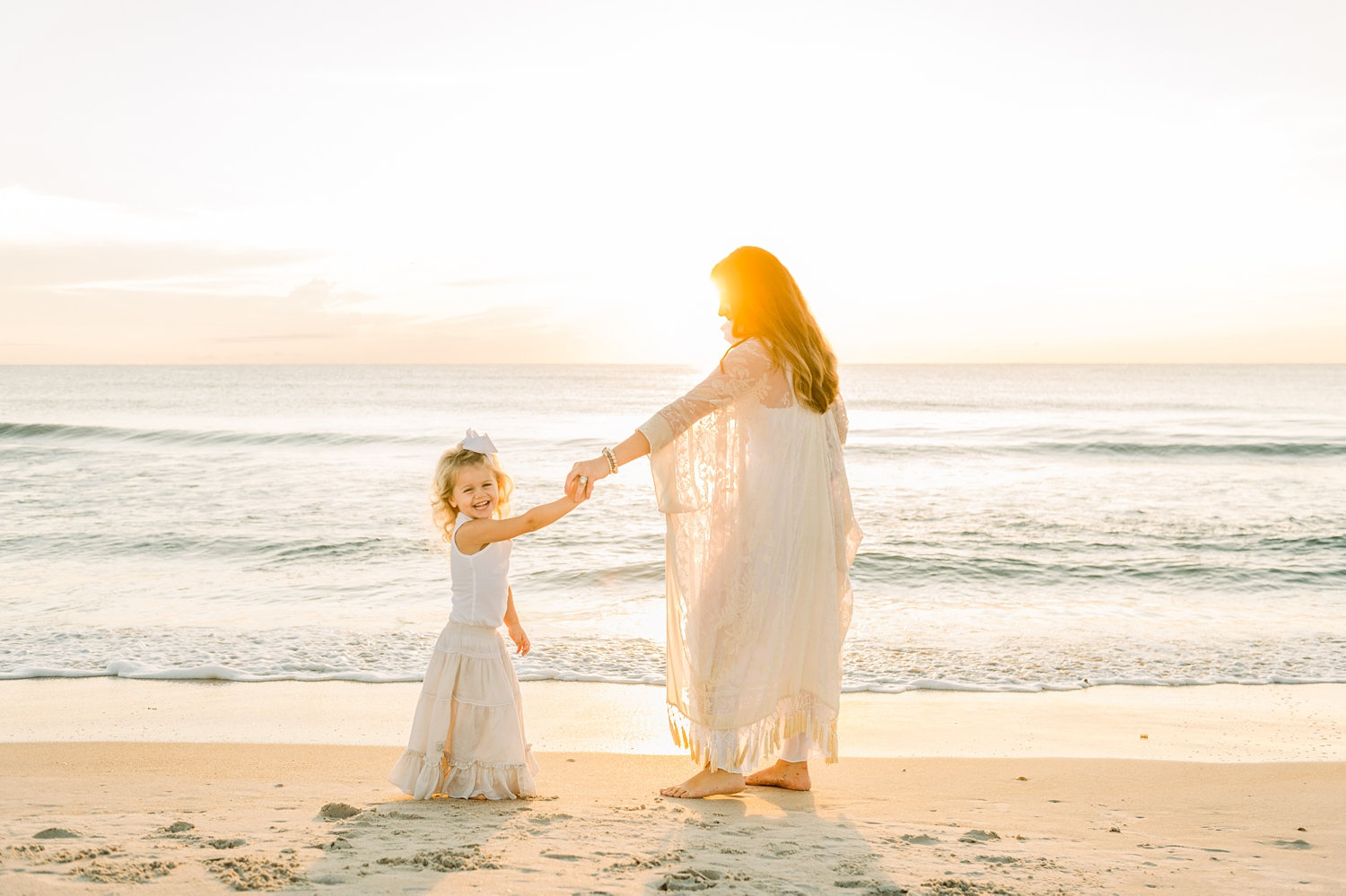 mother twirling her little girl on the beach, the little girl is smiling at the camera