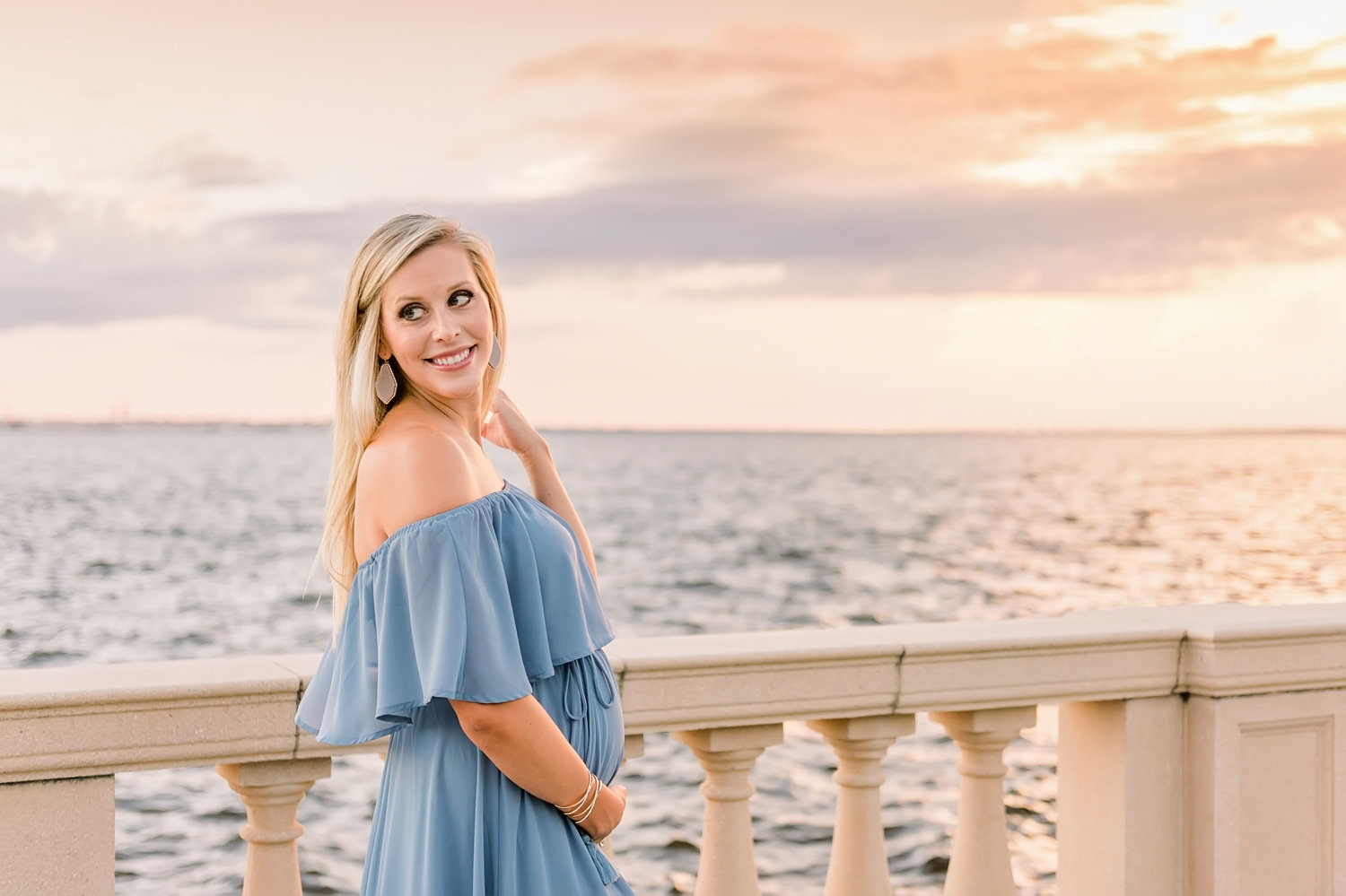 pregnant blonde woman smiling over her shoulder, old world architectural elements and the ocean behind her