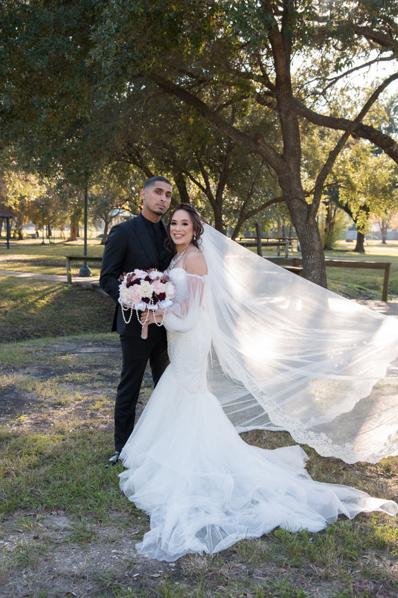 Wedding couple posing in park with veil flowing