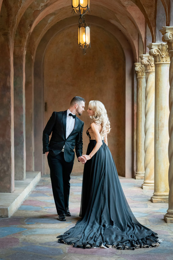 Elegant couple in formal attire holding hands in a stunning historic architecture setting.