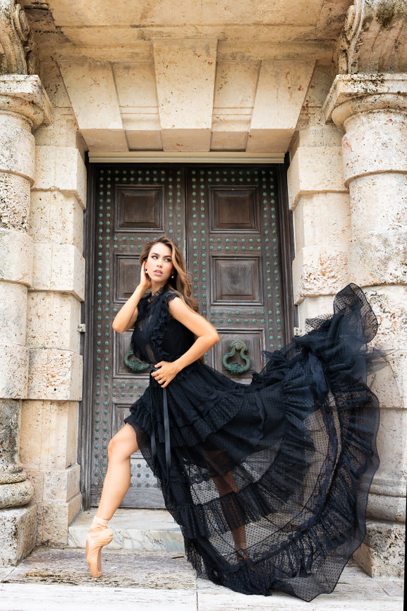 Ballerina in a flowing black dress poses gracefully in front of ornate stone doors.