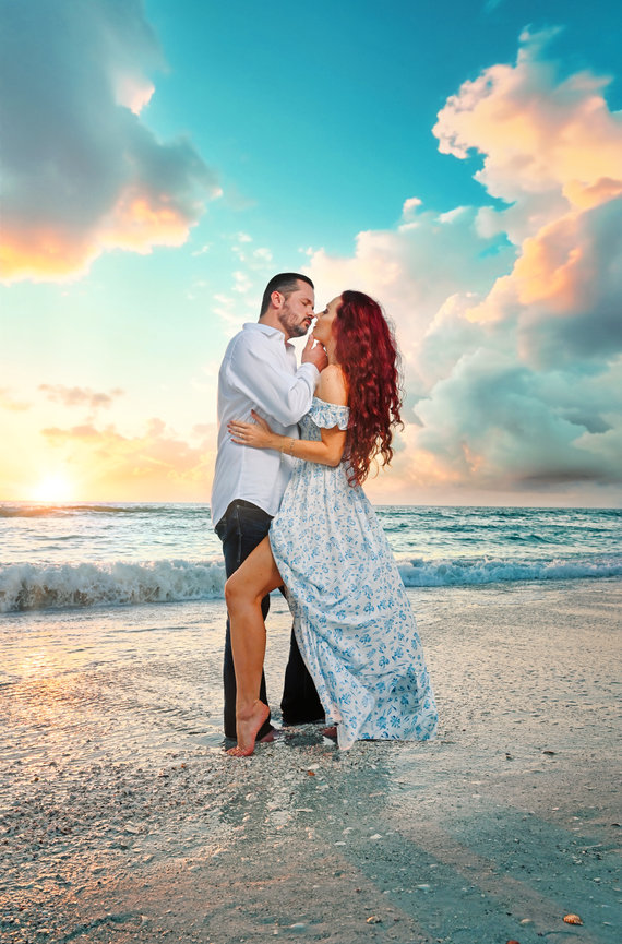 Couple embracing on a beach at sunset, with waves and colorful clouds in the background.