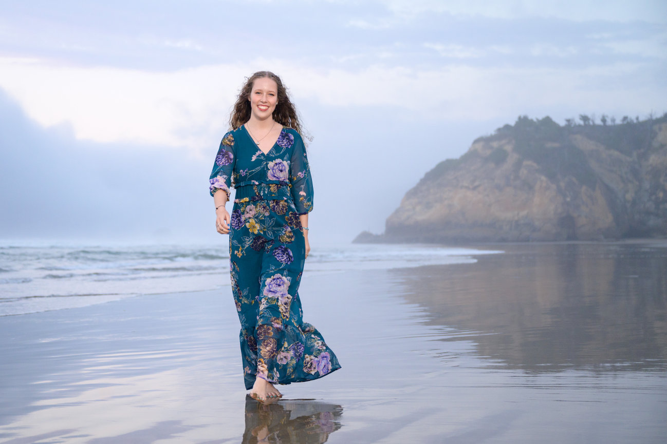 Senior girl wearing a blue floral dress walking along the ocean shore