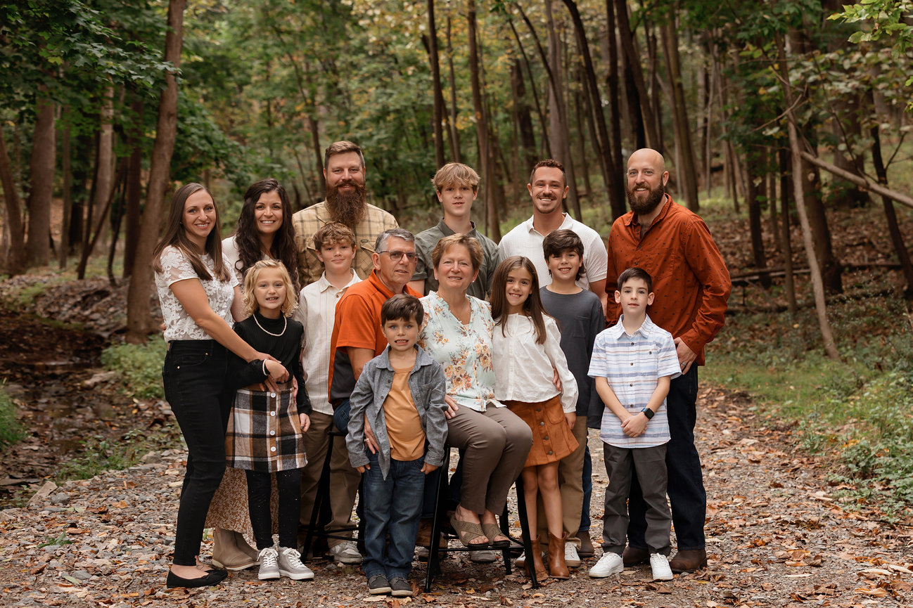 Family group posing outdoors on a forest path with autumn leaves. Adults and children are smiling.