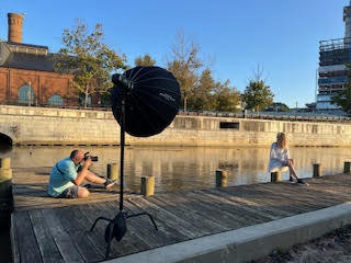Behind-the-scenes look at Master Photographer Ty Swartz photographing senior Sydney during a fine art session at a Texas waterfront location with portable softbox lighting, Swartz Portraits in Spring TX serving The Woodlands and Conroe
