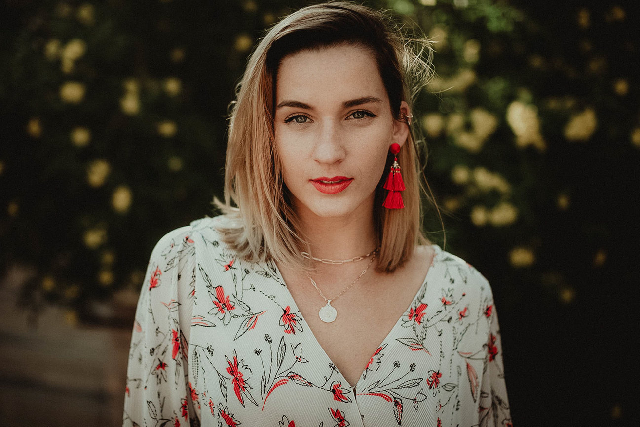 Beautiful and stylish photography portrait taken outdoors amongst yellow flowers and green bush with client wearing bold orang red lipstick and hip floral button up., portrait picture taken by Adam Trujillo, a Las Vegas portrait photographer.