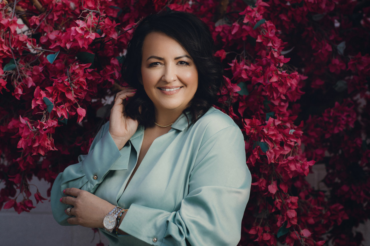 Pink flowers and a gorgeous portrait of Christina Vela in soft blue outfit and glowing smile. Professional picture taken by Adam Trujillo, a Las Vegas studio portrait photographer.