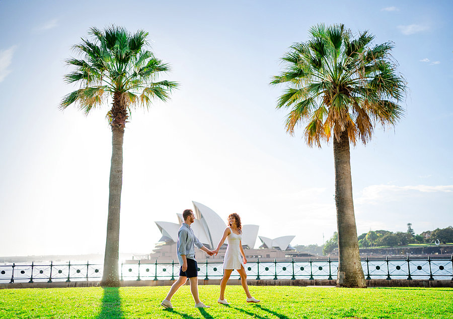 A romantic photoshoot with a couple walking in a park with the Sydney Opera House in the background.