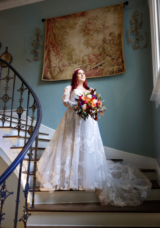 Bride descending a grand staircase with ornate railings, showcasing her lace wedding gown and floral bouquet captured by Fairhope Wedding photographer Dixon Creative Images
