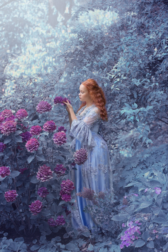 Woman in a flowing dress standing in a garden with purple flowers