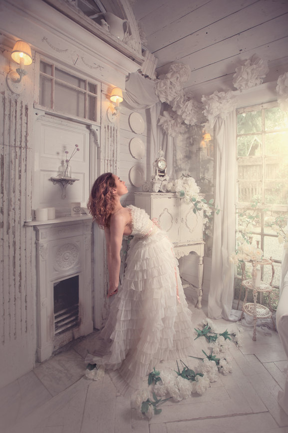 Woman in a white dress leaning against a fireplace in a decorated room