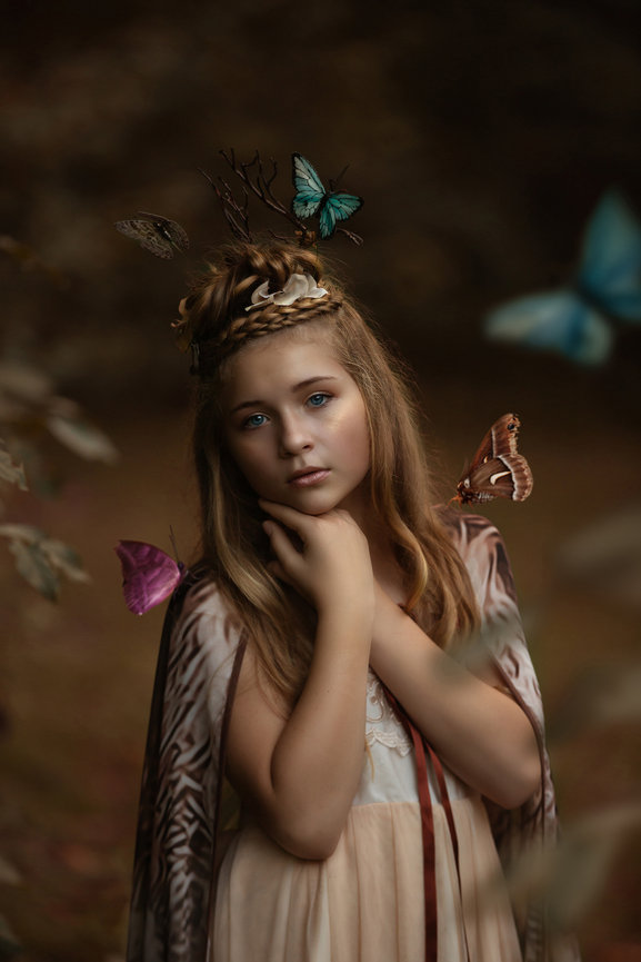 Girl with butterflies around her head standing in nature