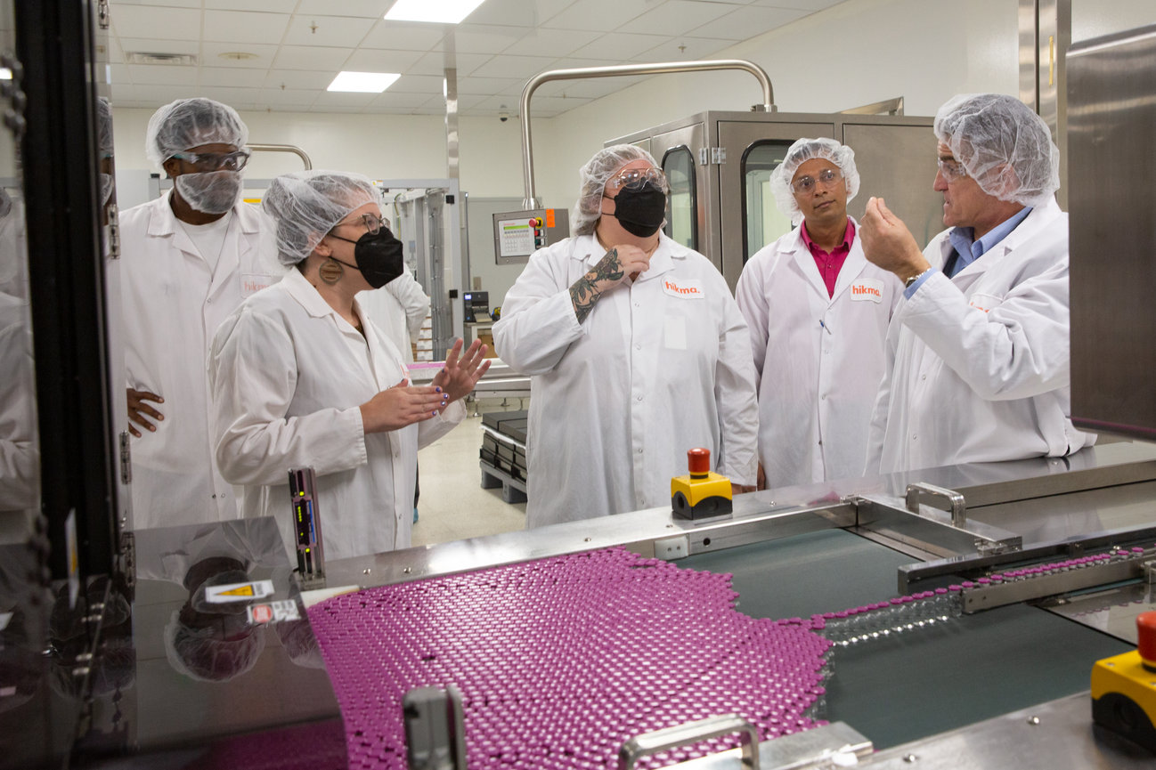 People in lab coats and hairnets observe a production line with pink items in a factory setting.