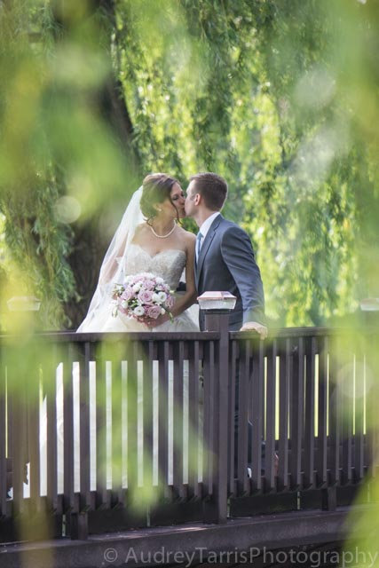 Bride and groom embracing on a bridge beneath hanging willow branches