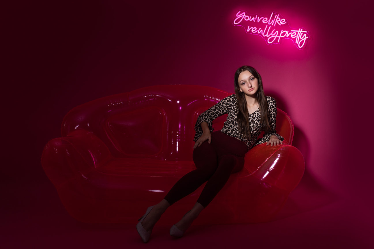 High School girl sitting on pink couch neon sign You're like really pretty  Denton