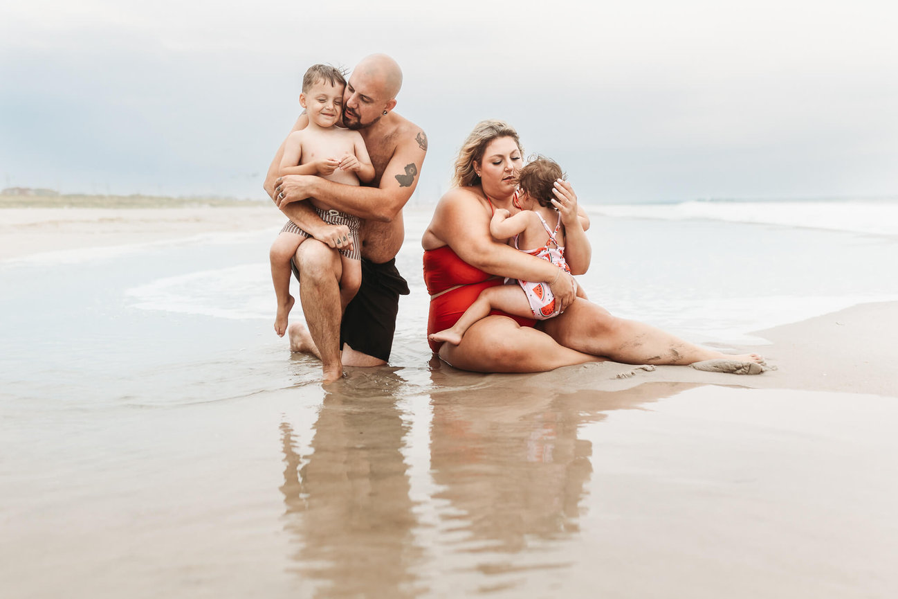 A family sitting in the water at the beach in Seaside Park, New Jersey during a family photo session.