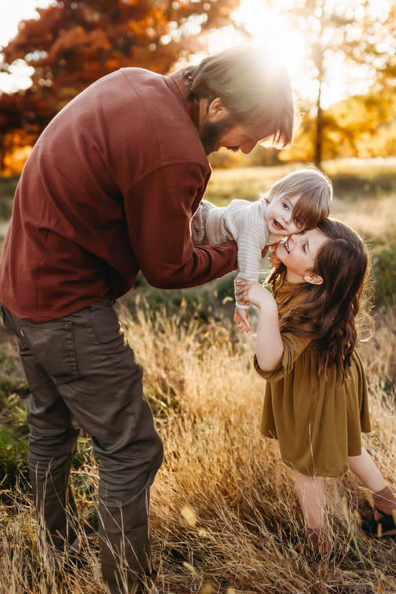 A father playing with his daughter and son in a field at the Central Park of Morris County during their family photo session.
