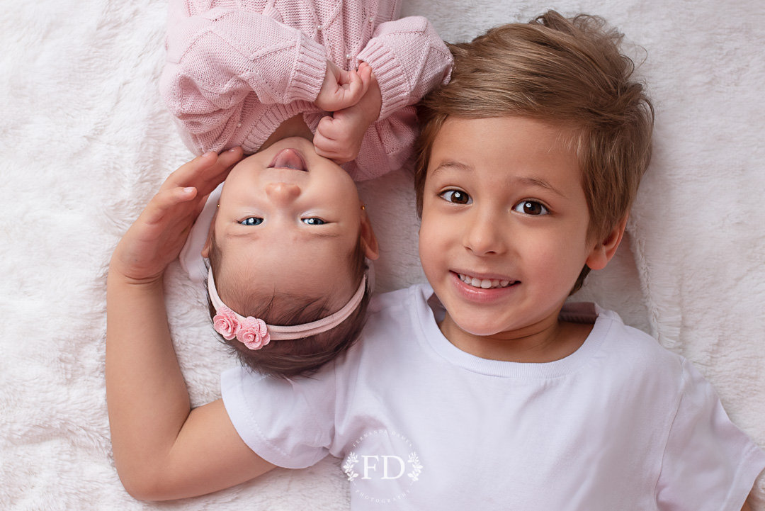 Toddler boy next to his baby sister sticking her tongue out