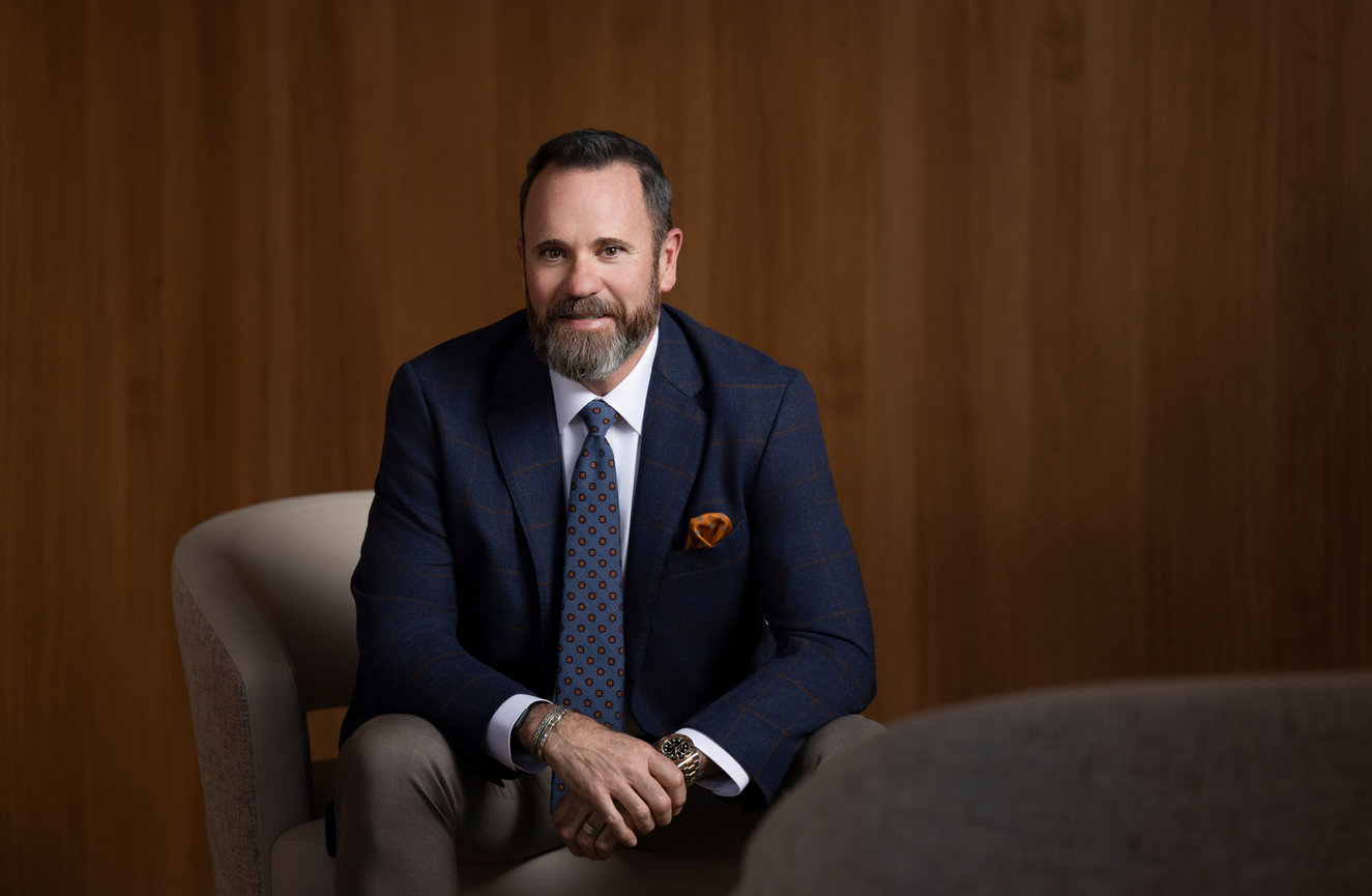 Bearded man in a suit seated in a formal office setting.