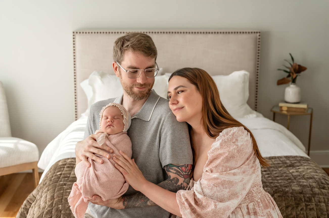 Parents holding sleeping newborn on a bed in a cozy bedroom- San Diego studio Hillcrest