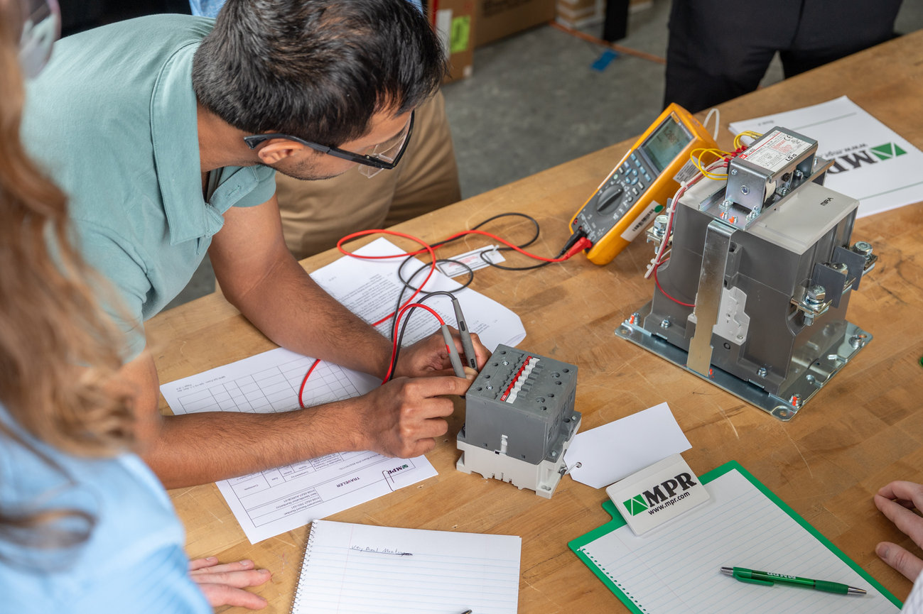 Person testing electrical equipment with a multimeter at a workshop table