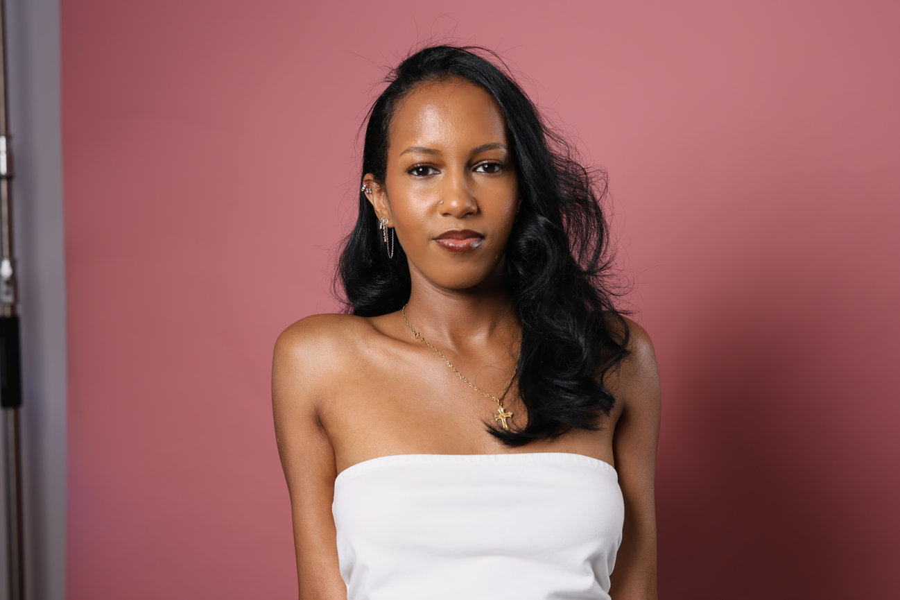 Portrait of a woman in a white top standing against a pink wall.