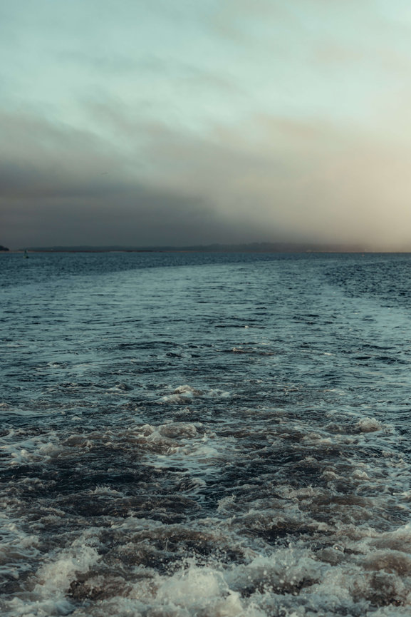 Calm ocean waves under a cloudy sky at sunset.