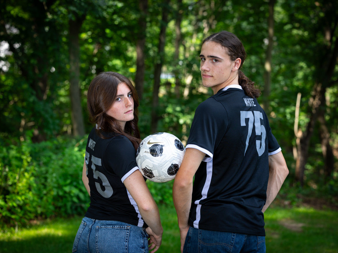 Teen couple posing with a soccer ball in a wooded outdoor setting.