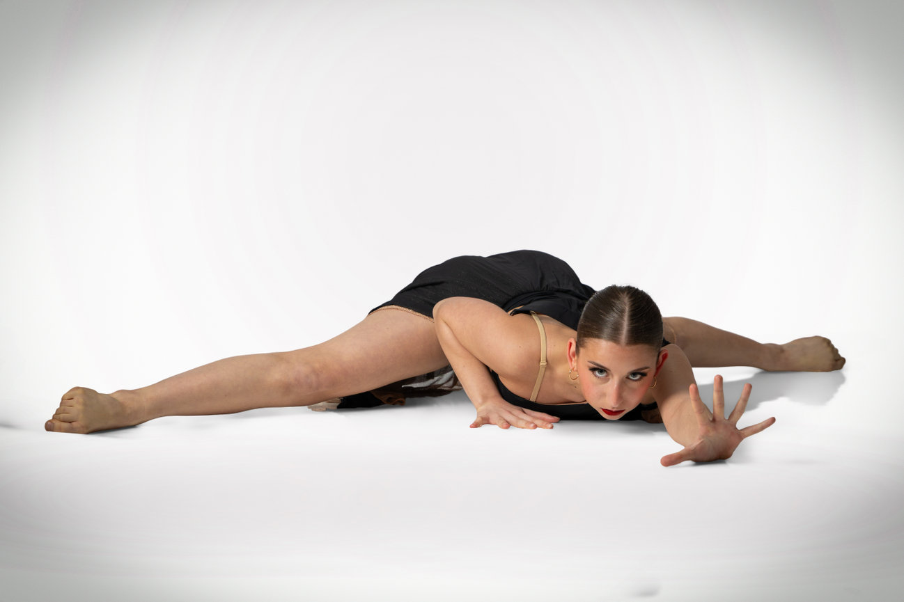 Dancer stretching low across a white studio floor in a dramatic pose.