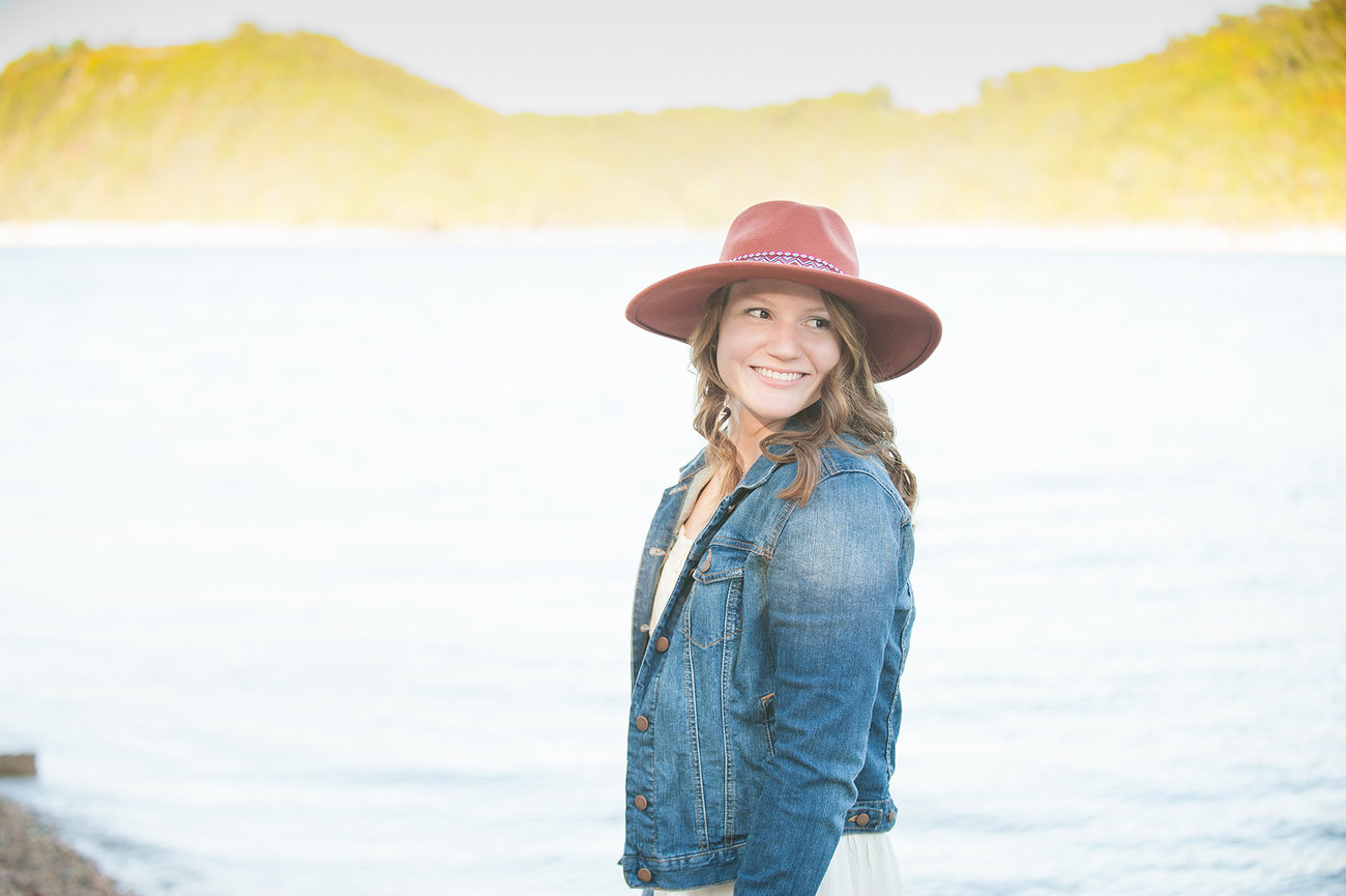 beautiful senior girl with coral hat and jean jacket looking over her shoulder for senior photo at Table Rock Lake