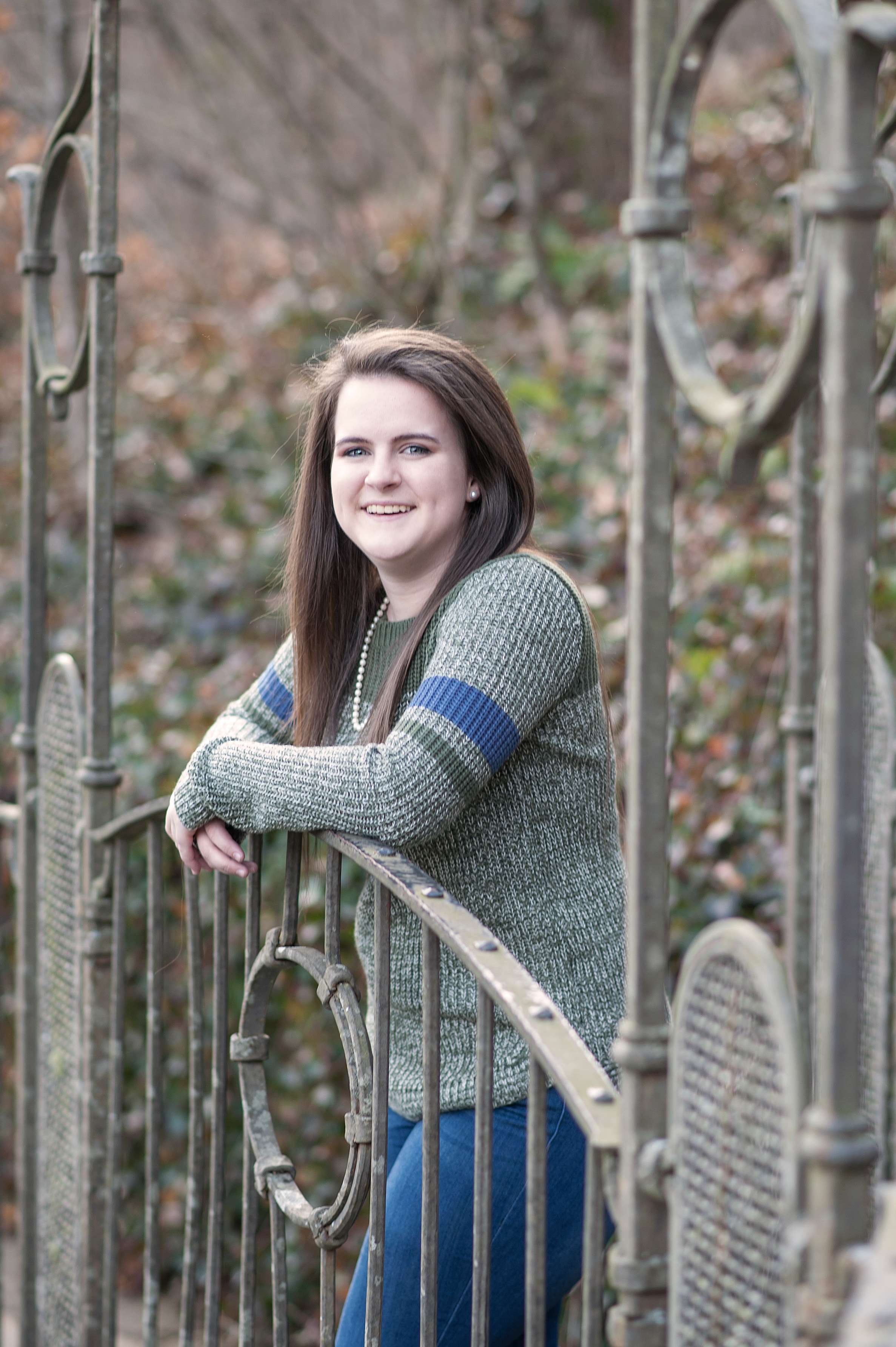 senior girl standing behind metal railing at Dogwood Canyon waterfall