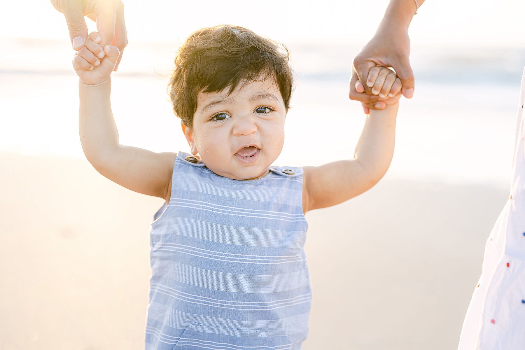 Indian baby boy smiling on beach wearing blue striped overalls
