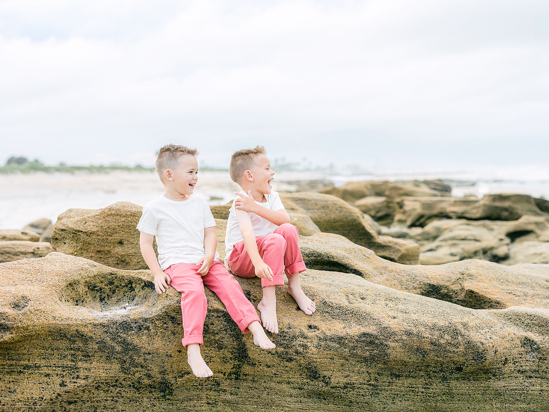 brothers sitting on rocks in pink pants on the beach
