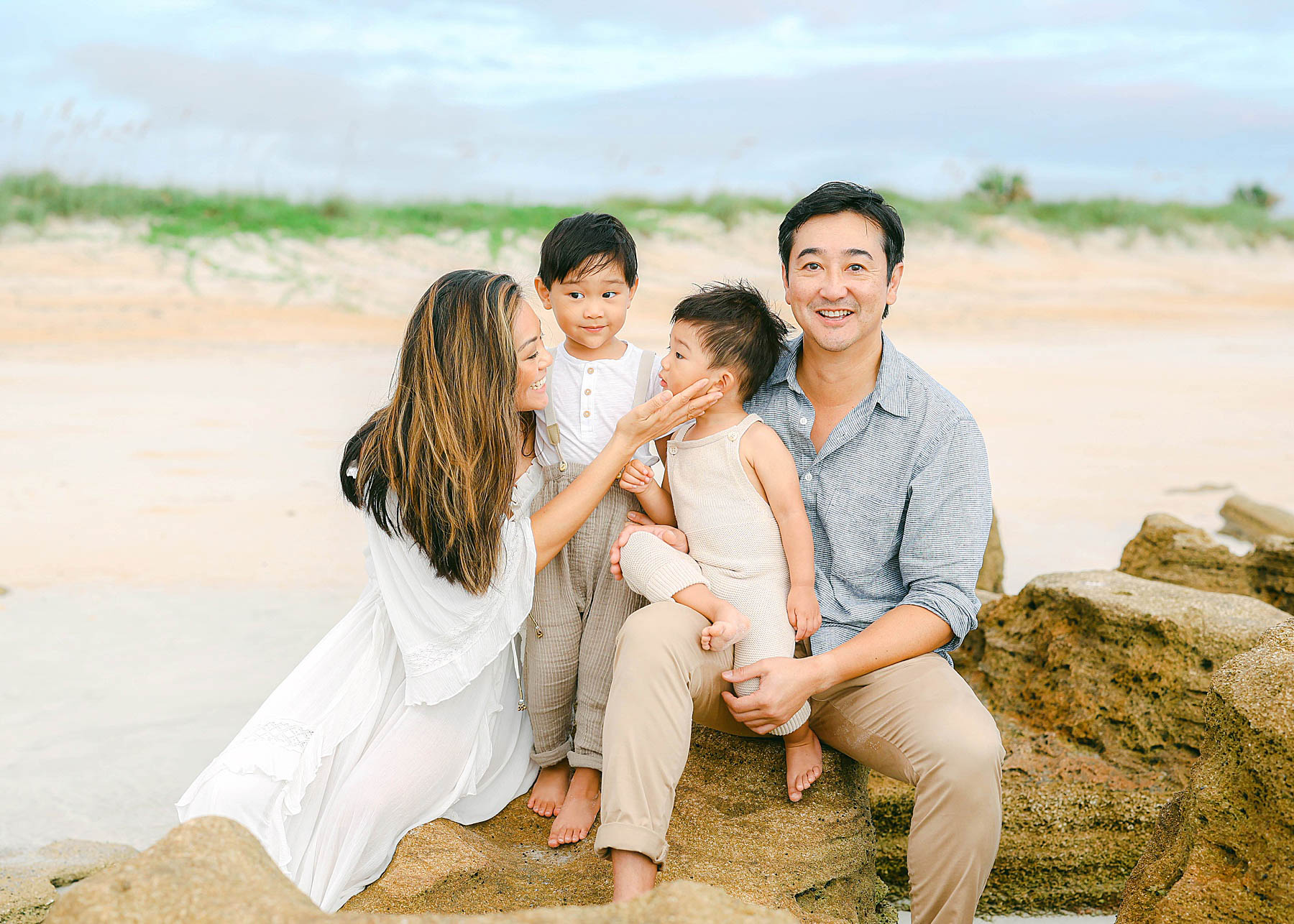 family sitting on a rock at the beach in neutral colors