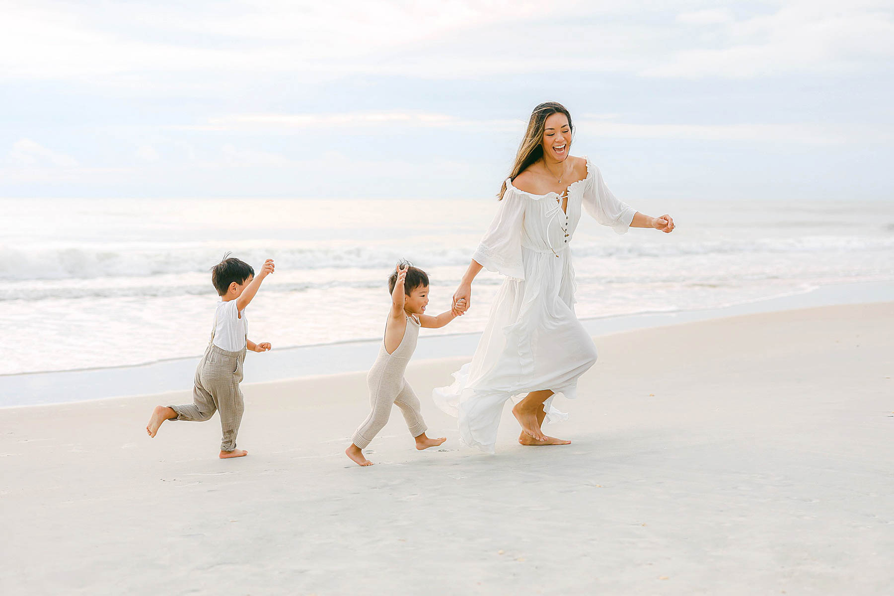 mom running with her kids on the beach in white dress