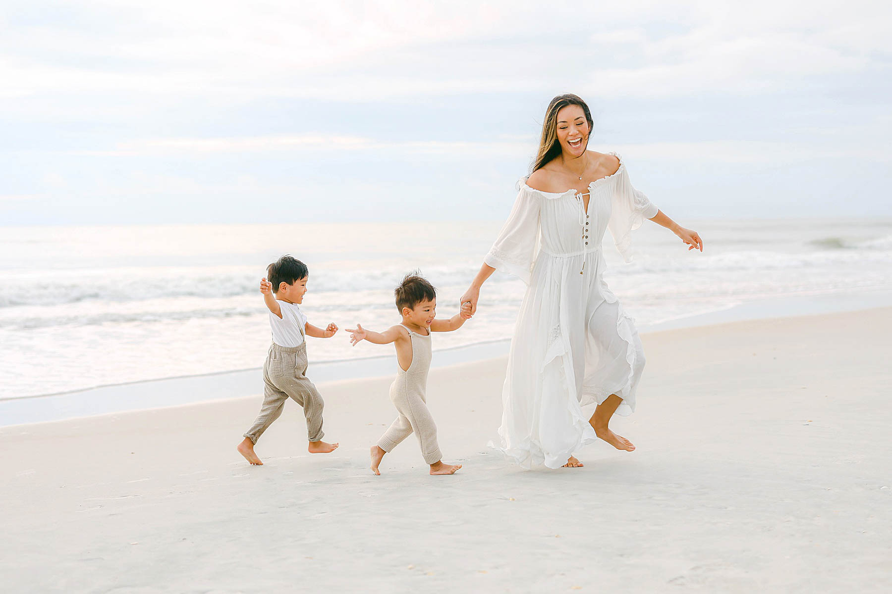 woman running on the beach in a white dress playing with two baby boys