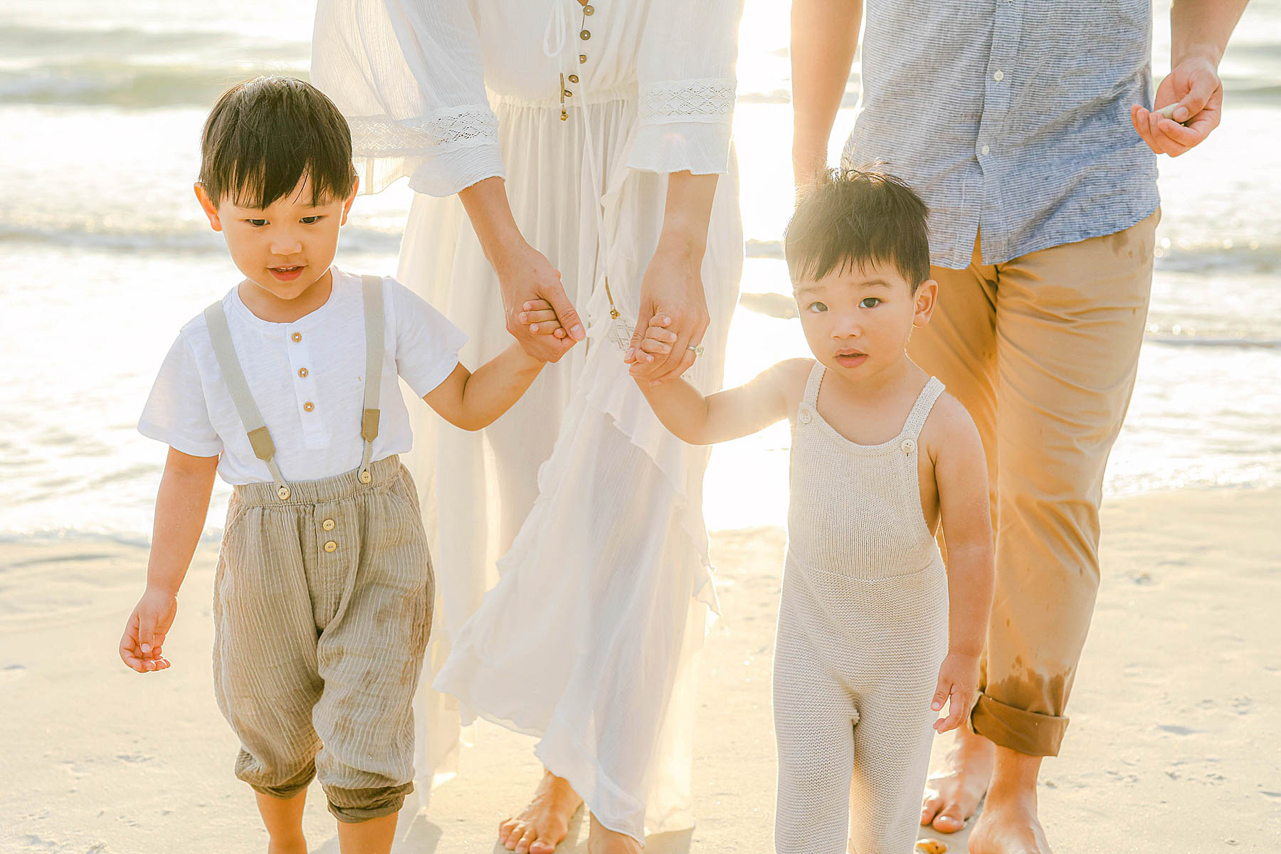 little boys holding each other hands in neutral colors on the beach
