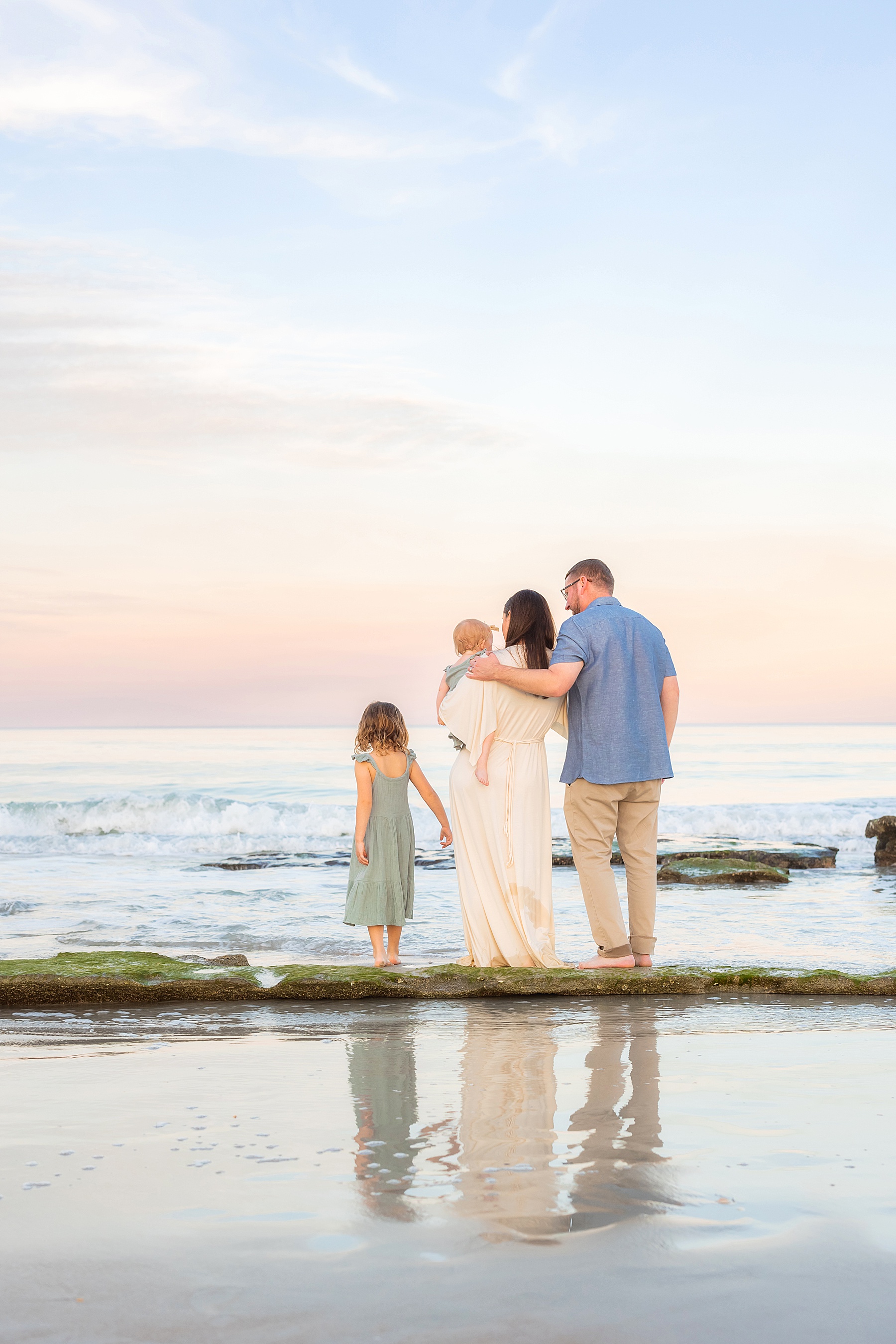 family standing in the pastel waters at the beach in florida on the rocks