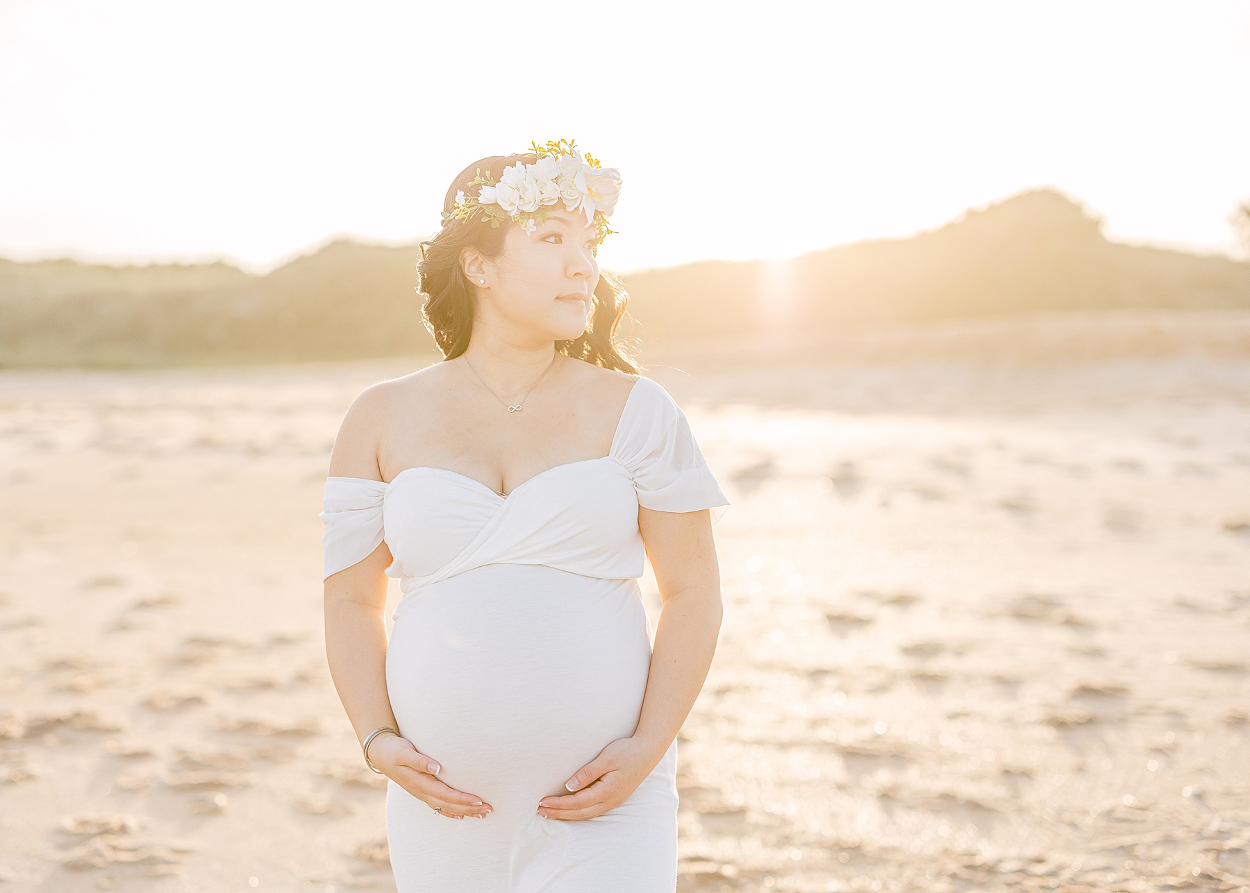pregnant woman wearing white long dress on the beach at sunset