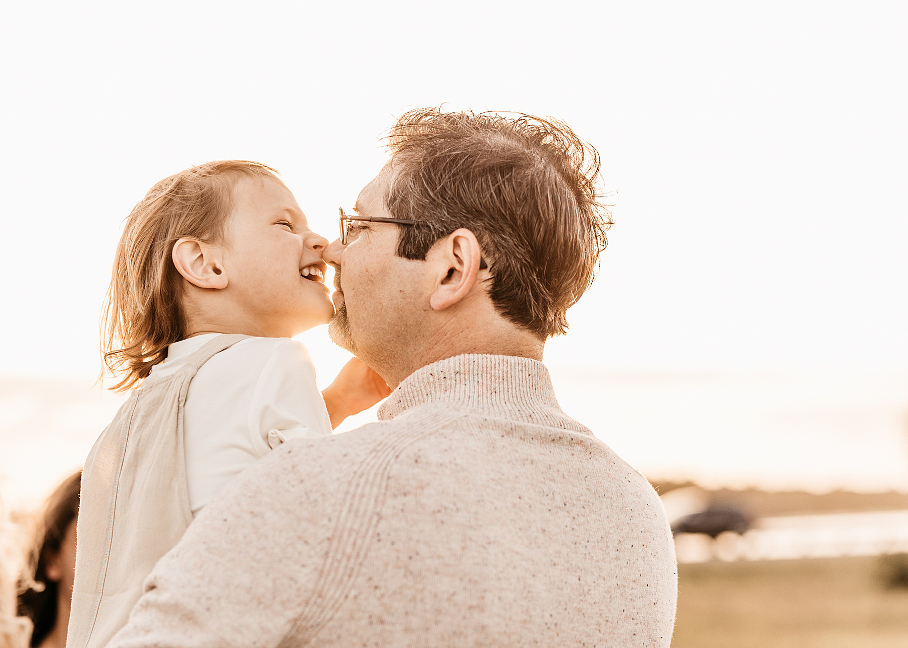 man laughing with little boy in open field dressed in neutral colors