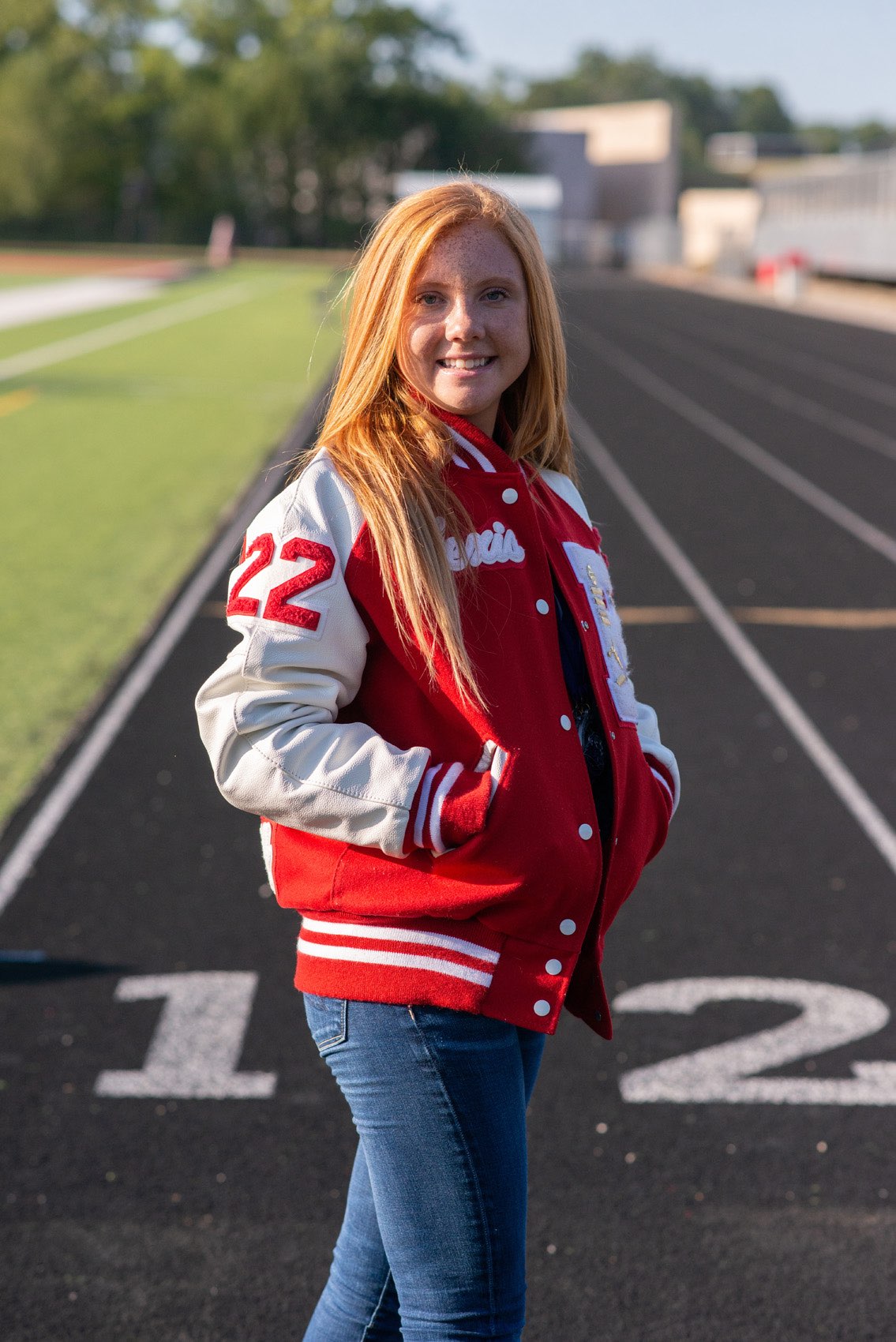 Senior girl in a letterman jacket standing on a track at her high school.
