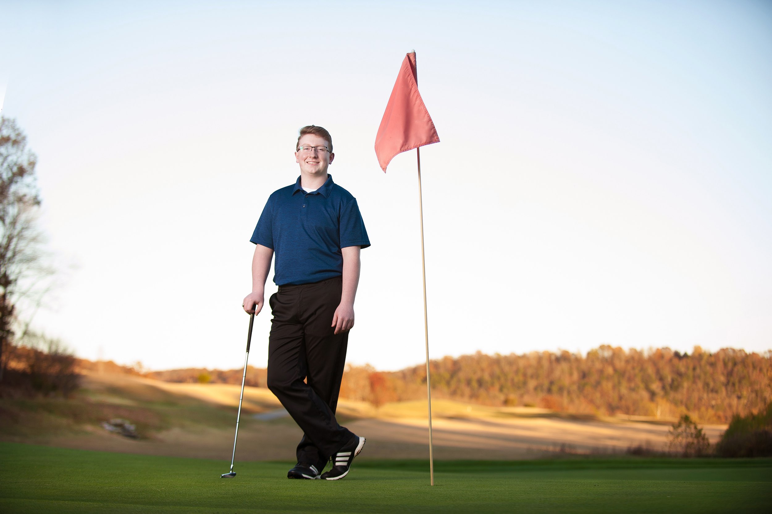 Golf player standing on green of golf course with sun setting.