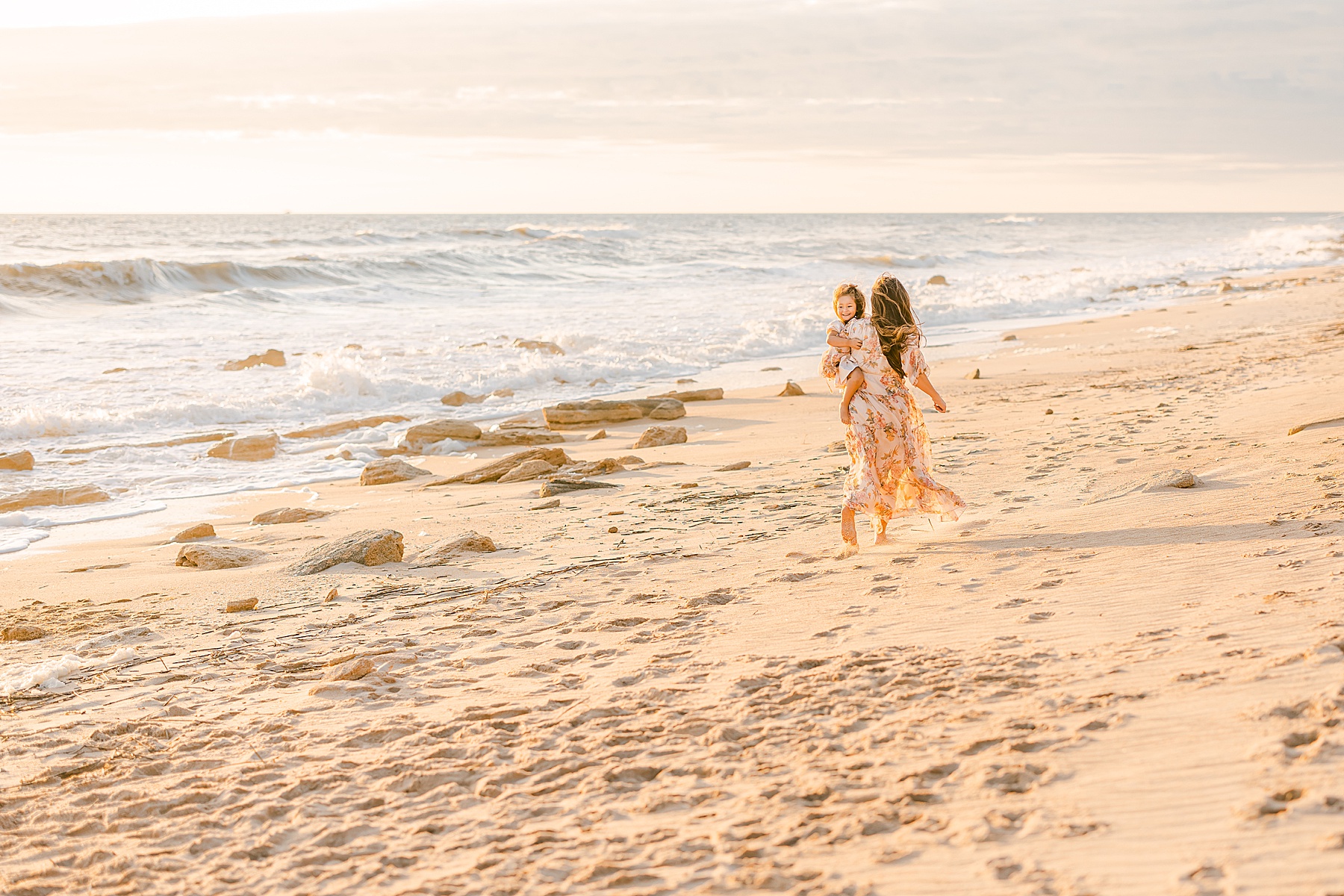 woman in peach and green floral dress walking with little girl on the beach at sunrise